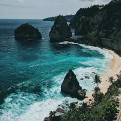 Turkusowe morze obmywa piaszczystą plażę z palmami. Klify porośnięte zielenią. Marzenie o tym, ile się leci na Bali.