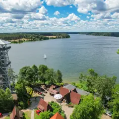 Wieża widokowa nad jeziorem, gdzie są Kaszuby. Żaglówka na wodzie, las i zabudowania.