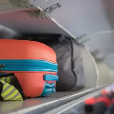 Pomarańczowa walizka i szara torba podróżna na półce bagażowej w samolocie Pegasus Airlines.