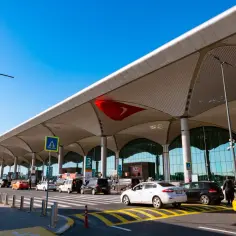 Nowoczesny terminal lotniska w Bodrum, z charakterystycznym dachem i ruchem samochodów przed wejściem.
