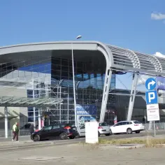 Nowoczesny budynek portu lotniczego Poznań-Ławica, z tablicą "PRZYLOTY ARRIVALS". Dobre opinie o tym lotnisku często dotyczą jego funkcjonalności.