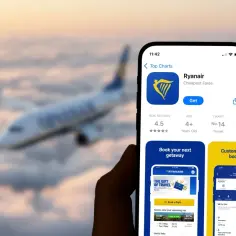 Dłoń trzyma smartfon z aplikacją Ryanair na tle samolotu lecącego nad chmurami.