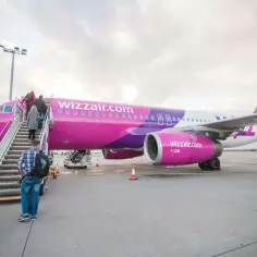 Różowy samolot Wizz Air z pasażerami wsiadającymi po schodkach na lotnisku.