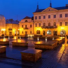 Wieczorny rynek w Piotrkowie Trybunalskim, mokry bruk odbija światła latarni. To piękne miejsce, gdzie można poczuć atmosferę miasta i odkryć jego atrakcje.