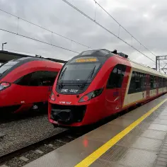 Dwa czerwono-kremowe pociągi SKM stojące na torach przy peronie.