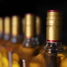 Rząd butelek z alkoholem, z błyszczącymi złotymi zakrętkami. Zastanawiasz się, czy można przewozić alkohol w bagażu rejestrowanym?