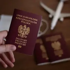 Dłoń trzyma polski paszport. Obok leżą kolejne dokumenty, maseczka i model samolotu. Zastanawiasz się, ile trzeba czekać na paszport?