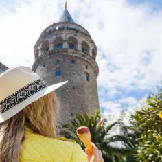Kobieta w kapeluszu z lodami podziwia wieżę Galata w Stambule, Turcja.