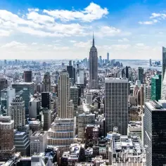 Widok na panoramę Nowego Jorku z wieżowcami, w tym Empire State Building, pod błękitnym niebem.