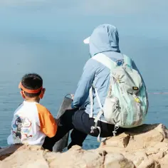 Chłopiec w pomarańczowej opasce i mama z plecakiem patrzą na morze. To idealny ekwipunek dla dziecka na wycieczkę.