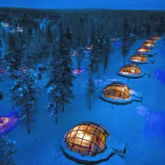 Szklane igloo w zaśnieżonym lesie, gdzie jest Laponia. Nocą rozświetlają je ciepłe światła, tworząc magiczny widok.