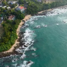 Widok z lotu ptaka na wybrzeże Sri Lanki. Widać domy, drogę, plażę i turkusowe morze. Czy Sri Lanka jest bezpiecznie? Tak, to piękny kraj do odwiedzenia.