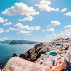 Santorini, Grecja. Białe domy z niebieskimi kopułami kościołów na zboczu góry, morze i chmury. Zastanawiasz się, ile się leci do Grecji?