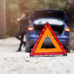 Trójkąt ostrzegawczy przed awaryjnym, niebieskim autem. Kobieta wzywa pomoc. PZU assistance holowanie do 1000 km.