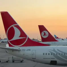 Samoloty Turkish Airlines na lotnisku. W tle widać wózki bagażowe i zachodzące słońce.