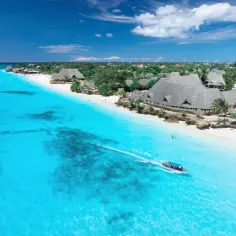 Zanzibar w lutym: błękitne morze, biała plaża i łódź z turystami. Idealna pogoda na wakacje.