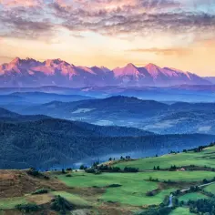 Widok na pasmo górskie o zachodzie słońca, z zielonymi wzgórzami w pierwszym planie.