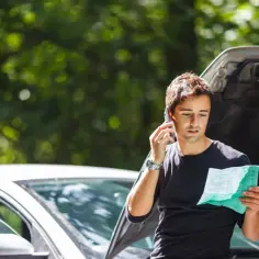 Mężczyzna z dokumentem w ręku dzwoni po assistance na wyjazd, gdy jego samochód uległ awarii.