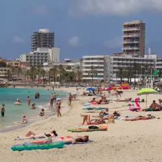 Słoneczna plaża na Majorce, majowa pogoda przyciąga tłumy plażowiczów. Ludzie kąpią się w turkusowej wodzie i opalają na piasku.