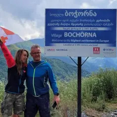 Para, z gruzińską flagą, na tle gór i znaku "Wioska Bochorna", najwyżej położona osada w Europie. Czy w Gruzji jest bezpiecznie? Tak!