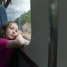 Dziewczynka wpatruje się przez okno pociągu, zastanawiając się, od ilu lat można jeździć samemu pociągiem.