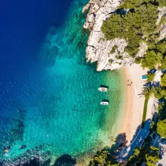 Idealne wakacje w Chorwacji: piaszczysta plaża, turkusowa woda, łodzie kołyszące się na falach i bujna zieleń.