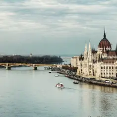 Budapeszt nad Dunajem, Parlament i most. W tle widać miasto, a na wodzie statek. Warto poznać walutę tego pięknego miasta.