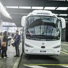 Grupa osób czeka na biały autobus Terravision przy peronie 3 na lotnisku w Mediolanie.