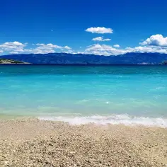 Idealne miejsce, gdzie na wakacje w czerwcu: turkusowe morze, kamienista plaża i góry w tle.