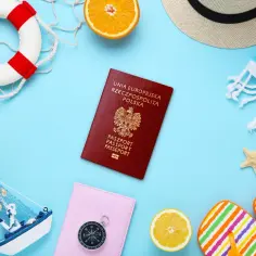 Polski paszport, dowód tożsamości strefy eog, leży obok plażowych akcesoriów: koła ratunkowego, muszli, kapelusza i klapków.