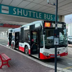 Autobus wahadłowy na lotnisko w Bari czeka na pasażerów. Czerwona ławka zaprasza do odpoczynku.
