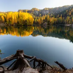 Jesienne barwy otaczają spokojną taflę wody w skalnym mieście w Czechach.