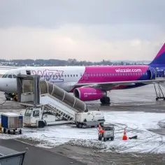 Samolot Wizz Air na lotnisku zimą, z drabiną i obsługą naziemną.