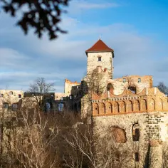Ruiny zamku na wzgórzu, jeden z największych zamków w Polsce, z wieżą i ceglanymi arkadami.