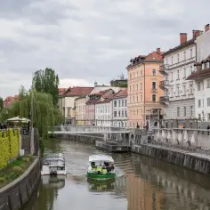 Łódki płyną rzeką w Lublanie, gdzie można podziwiać architekturę i poczuć atmosferę miasta, którego walutą jest euro.