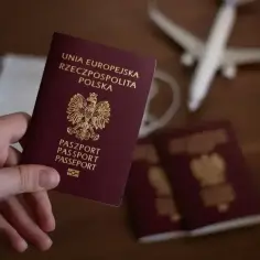 Dłoń trzyma polski paszport. Obok leżą inne paszporty, maseczka i samolot. Zastanawiasz się, ile się czeka na paszport?