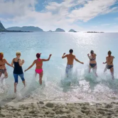 Grupa ludzi biegnie do wody na piaszczystej plaży. Zastanawiasz się, jakie ubezpieczenie turystyczne wybrać, by cieszyć się wakacjami bez obaw.