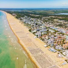 Słoneczna bibione plaża tętni życiem, pełna leżaków i turystów. W tle widać miasteczko i turkusowe morze.