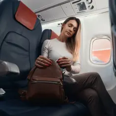 Kobieta w samolocie szuka czegoś w plecaku, zastanawiając się, czy w samolocie można ładować telefon.