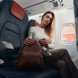 Kobieta w samolocie szuka czegoś w plecaku, zastanawiając się, czy w samolocie można ładować telefon.