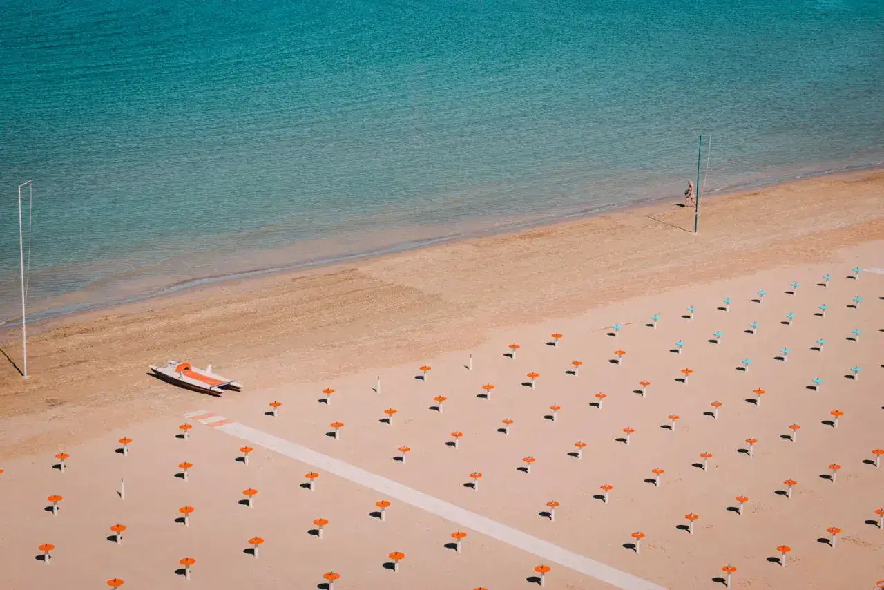 Pusta plaża w Rimini, z rzędem parasoli i łodzią ratunkową. Czy jest bezpiecznie? Wygląda na spokojnie.