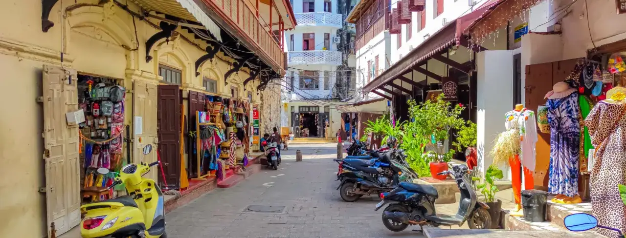 Uliczka na Zanzibarze z kolorowymi sklepikami, skuterami i manekinami w letnich strojach. Zastanawiasz się nad zanzibar ceny pamiątek?