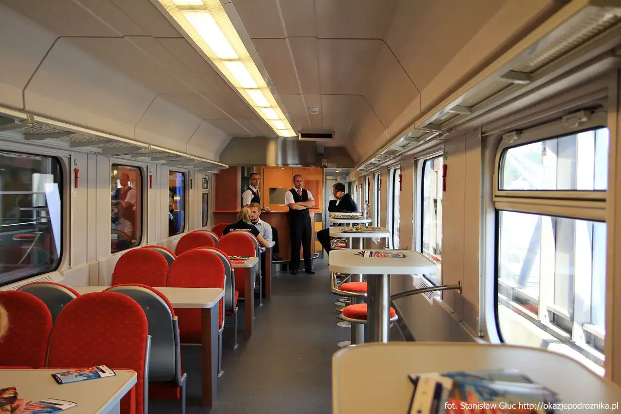 W wagonie restauracyjnym Intercity, gdzie można zjeść posiłek, siedzą pasażerowie, a obsługa przygotowuje zamówienia.