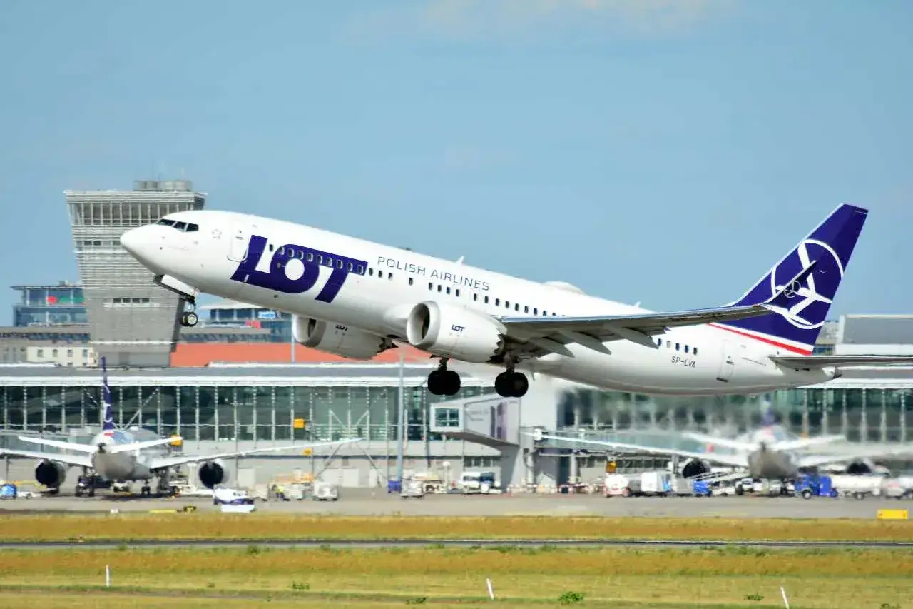 Samolot LOT Polish Airlines startuje, gotowy na loty do Malagi. W tle lotnisko i inne maszyny.
