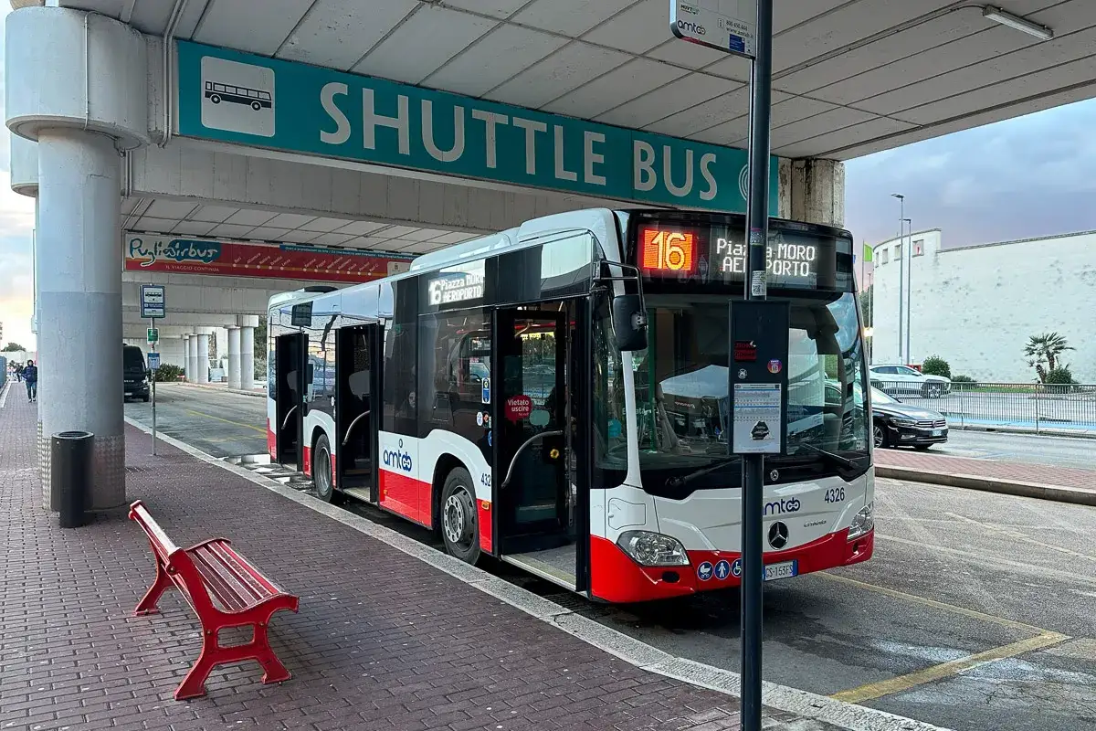 Autobus wahadłowy na lotnisko w Bari czeka na pasażerów. Czerwona ławka zaprasza do odpoczynku.