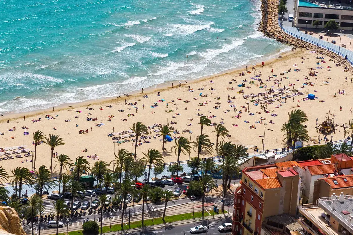 Słoneczna plaża w Alicante w marcu, pełna ludzi cieszących się ciepłą pogodą.