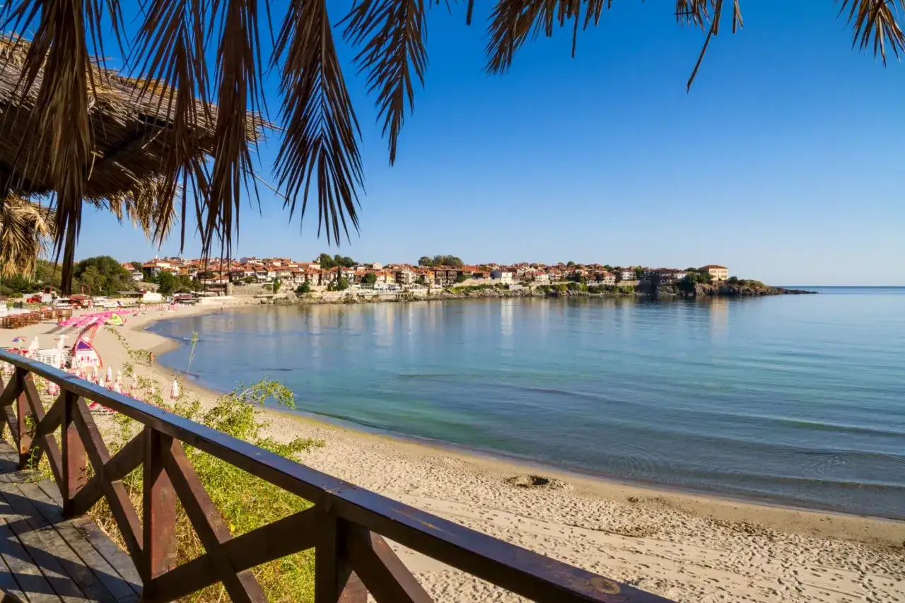 Słoneczny dzień na plaży w Bułgarii. Widok na zatokę z miasteczkiem w tle, palmy i drewniana balustrada. Idealne miejsce na wakacje.