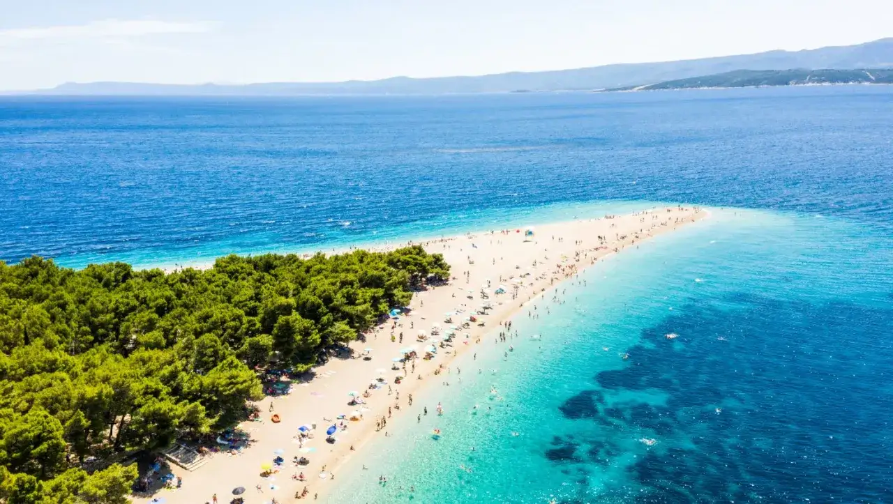 Rajski widok na plażę Zlatni Rat, idealne miejsce na wakacje w Chorwacji. Tłumy ludzi cieszą się słońcem i krystalicznie czystą wodą.