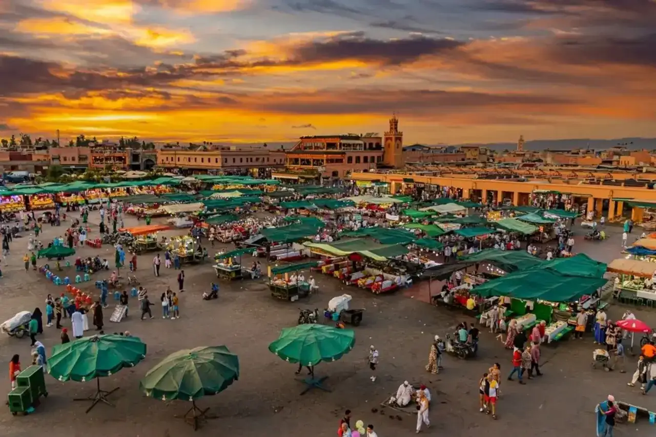 Tętniący życiem plac w Marrakeszu o zachodzie słońca. Tłumy ludzi spacerują między straganami pod zielonymi parasolami. Czy Maroko jest bezpieczne? Ten widok sugeruje, że tak, pełne życia i energii.