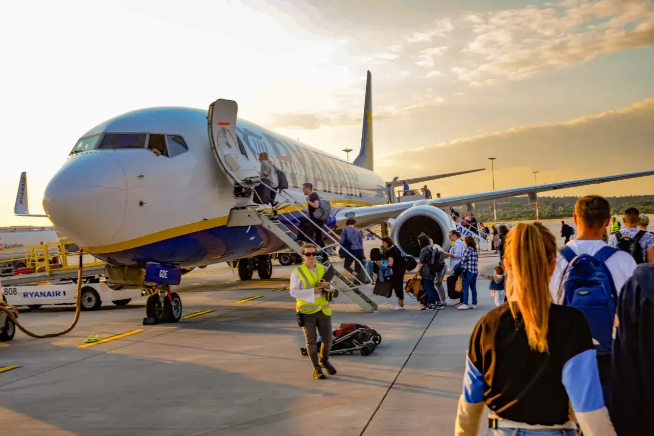 Pasażerowie wsiadają do samolotu Ryanair, popularnych hiszpańskich linii lotniczych, na tle zachodzącego słońca.